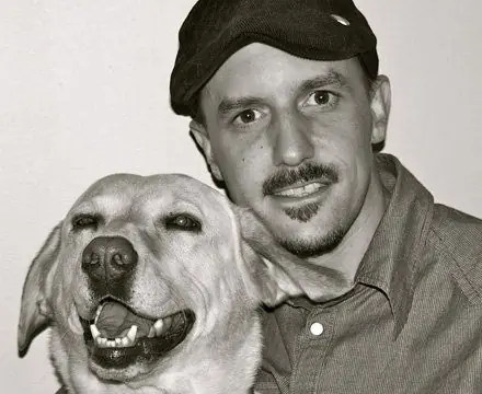 Black-and-white portrait of a man in a flat cap with a yellow Labrador